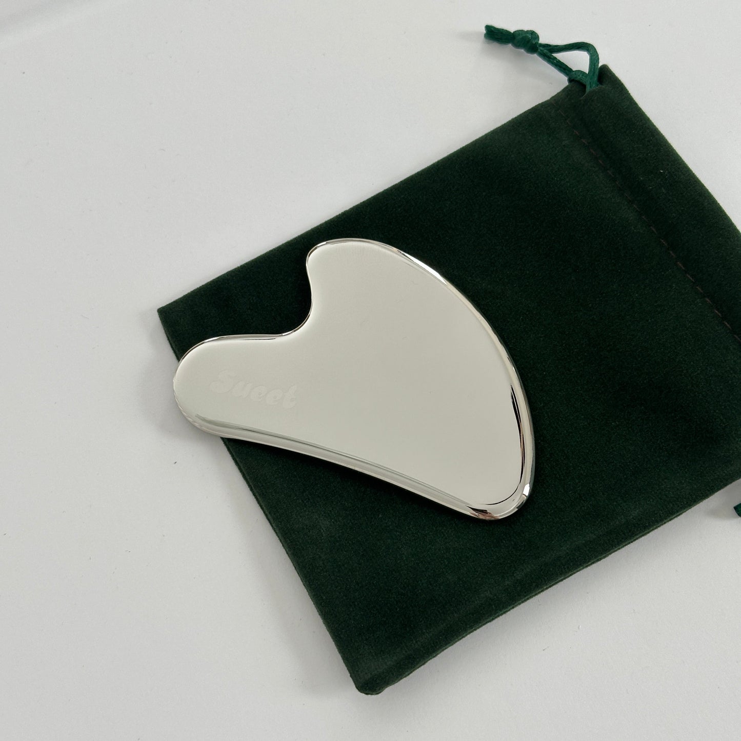 Silver gua sha tool on a black velvet pouch against a white background
